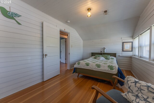 bedroom with wood walls, wood finished floors, and vaulted ceiling