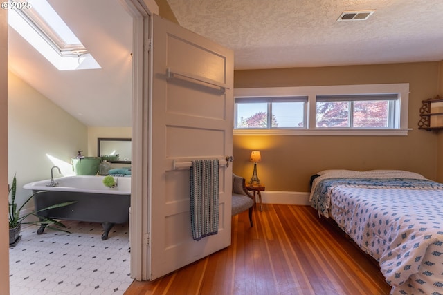 bedroom with baseboards, visible vents, lofted ceiling with skylight, and hardwood / wood-style floors