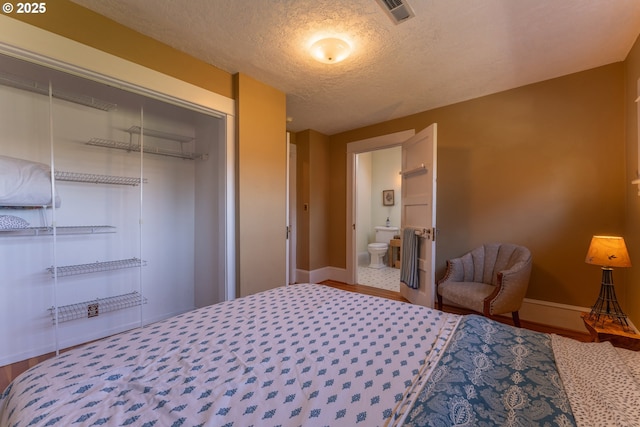 bedroom with a textured ceiling, baseboards, wood finished floors, visible vents, and a closet