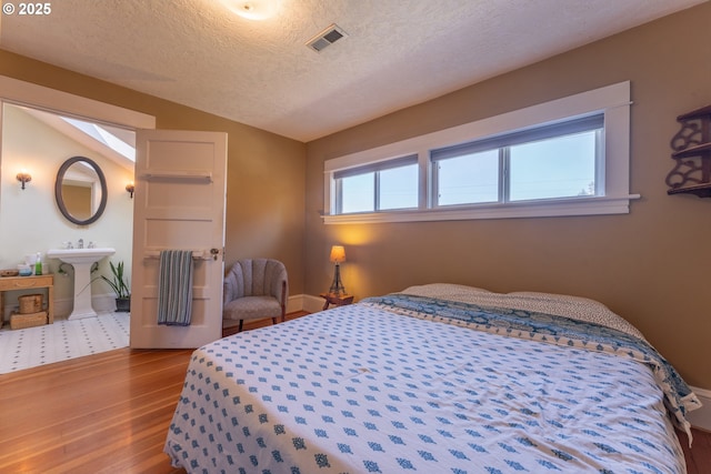 bedroom with a textured ceiling, visible vents, wood finished floors, baseboards, and lofted ceiling