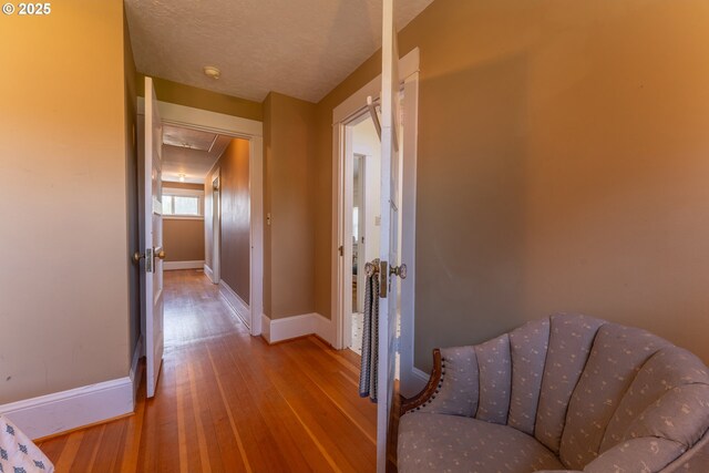 hallway with baseboards, attic access, and hardwood / wood-style flooring