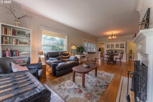 living room featuring ornamental molding, a fireplace with flush hearth, wood finished floors, and a notable chandelier