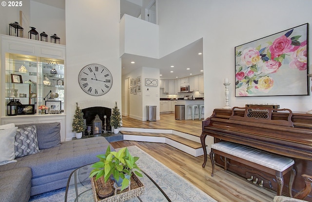 living room featuring a warm lit fireplace, light wood finished floors, and a high ceiling