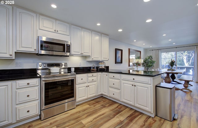 kitchen with stainless steel appliances, a peninsula, white cabinetry, light wood finished floors, and dark countertops