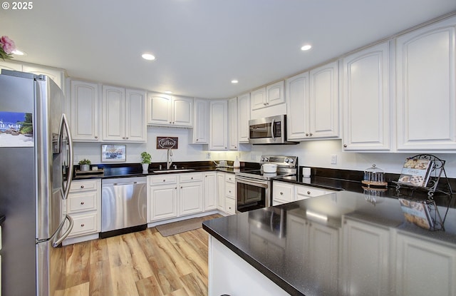 kitchen with appliances with stainless steel finishes, a sink, light wood-style flooring, and white cabinetry