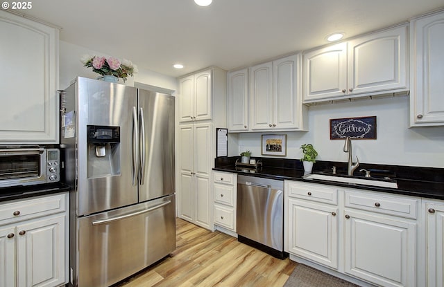 kitchen with stainless steel appliances, dark countertops, a sink, and white cabinetry