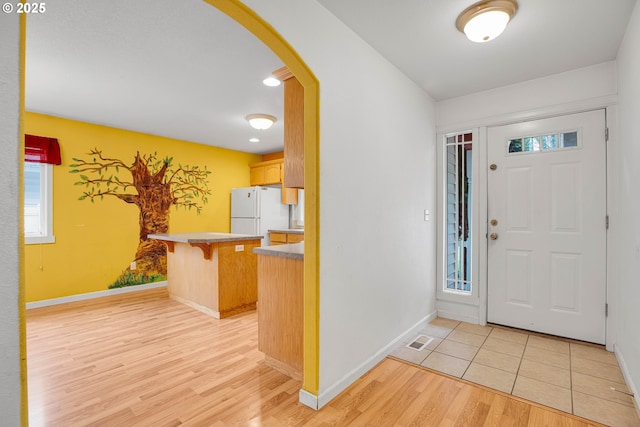 entryway featuring arched walkways, light wood-type flooring, and baseboards