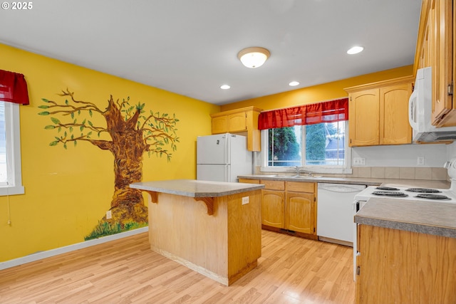 kitchen with white appliances, light wood-style flooring, a sink, a kitchen bar, and a center island