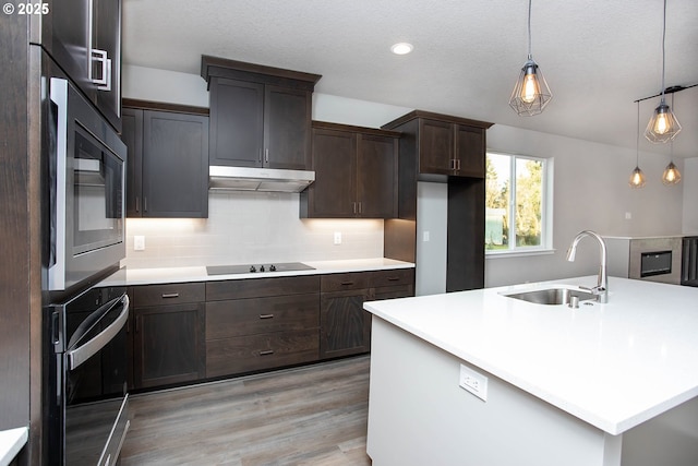 kitchen with pendant lighting, sink, tasteful backsplash, an island with sink, and oven