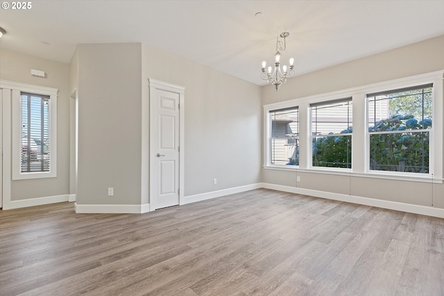 spare room with light hardwood / wood-style flooring, an inviting chandelier, and a wealth of natural light