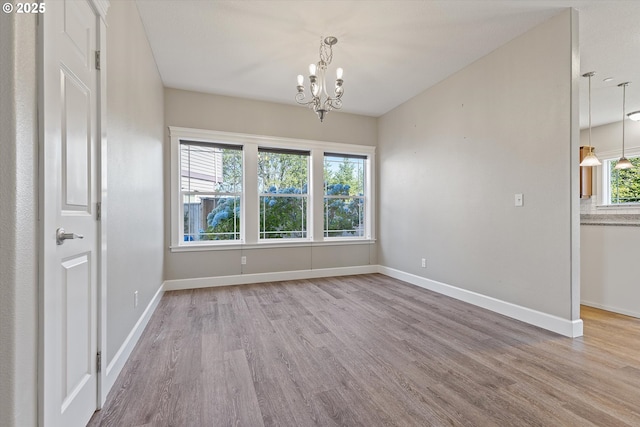 unfurnished room with a healthy amount of sunlight, light hardwood / wood-style floors, and an inviting chandelier