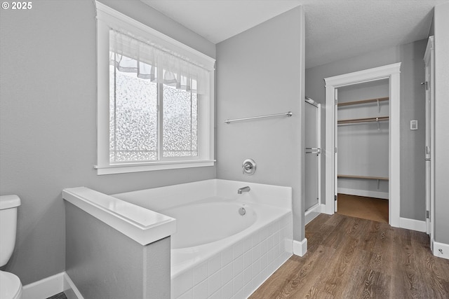 bathroom with a relaxing tiled tub, toilet, and hardwood / wood-style flooring