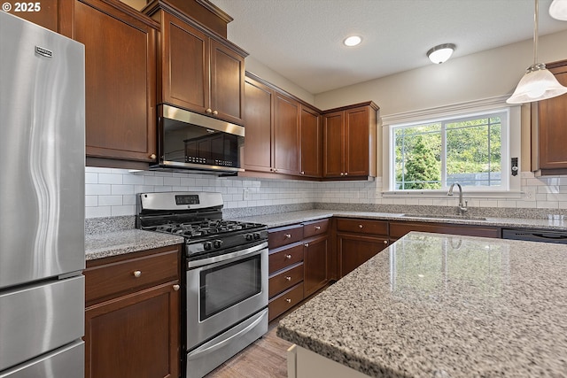 kitchen featuring light stone countertops, sink, stainless steel appliances, decorative light fixtures, and decorative backsplash