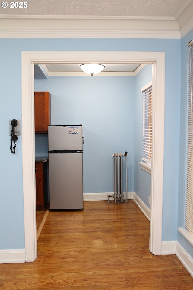 hallway with radiator, light wood-style flooring, baseboards, and crown molding