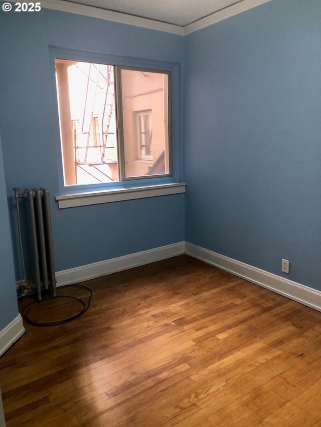 unfurnished room featuring radiator, crown molding, baseboards, and wood finished floors