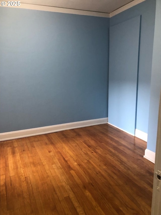 spare room featuring baseboards, wood finished floors, and crown molding