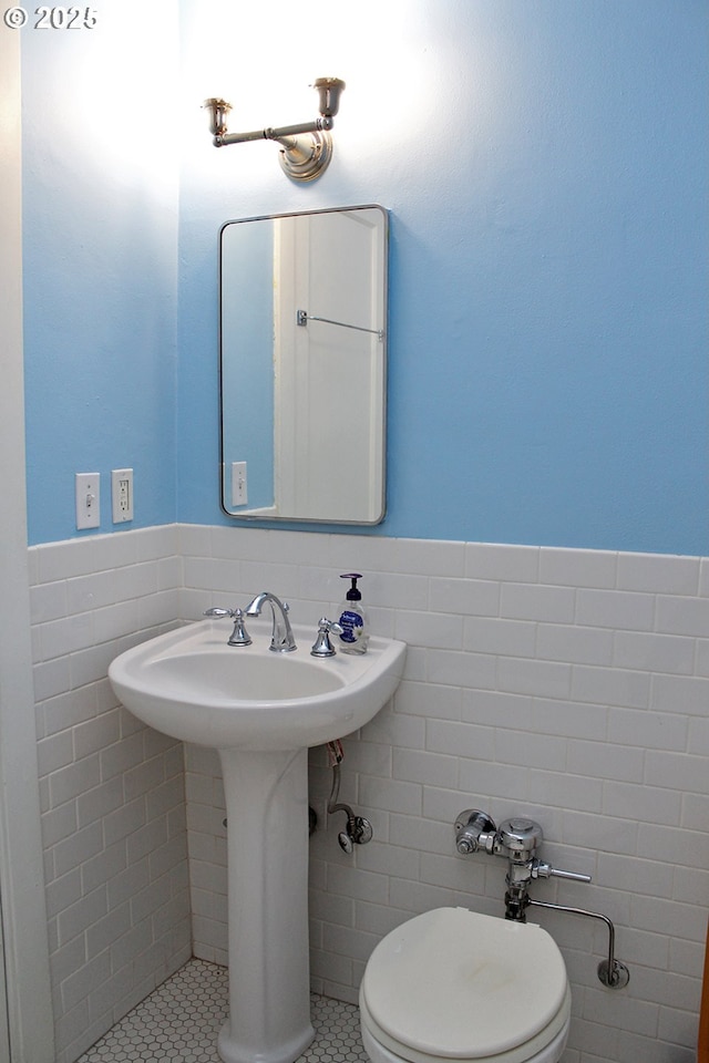 half bath with toilet, wainscoting, tile walls, and tile patterned floors