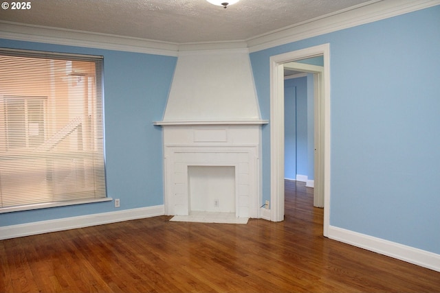 unfurnished living room featuring a textured ceiling, ornamental molding, wood finished floors, and baseboards