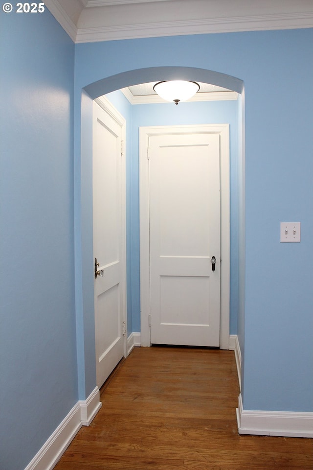 hallway with arched walkways, crown molding, baseboards, and wood finished floors