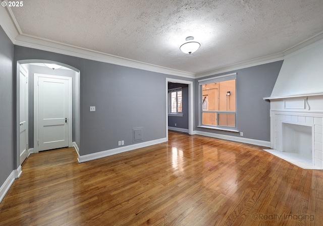 709 SW 16th Ave Unit 105, Portland, OR 97205 - unfurnished living room featuring a textured ceiling, wood finished floors, crown molding, arched walkways, and a tile fireplace