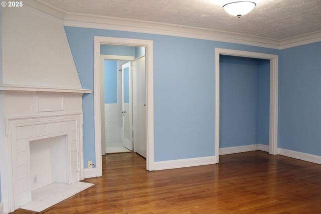 unfurnished living room featuring a tiled fireplace, ornamental molding, a textured ceiling, wood finished floors, and baseboards