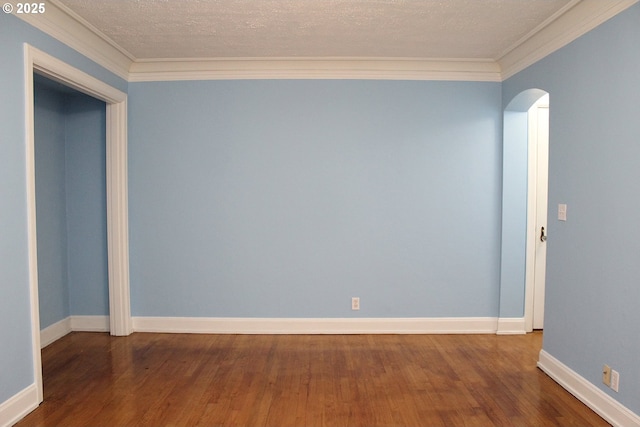 spare room with arched walkways, a textured ceiling, wood finished floors, and crown molding