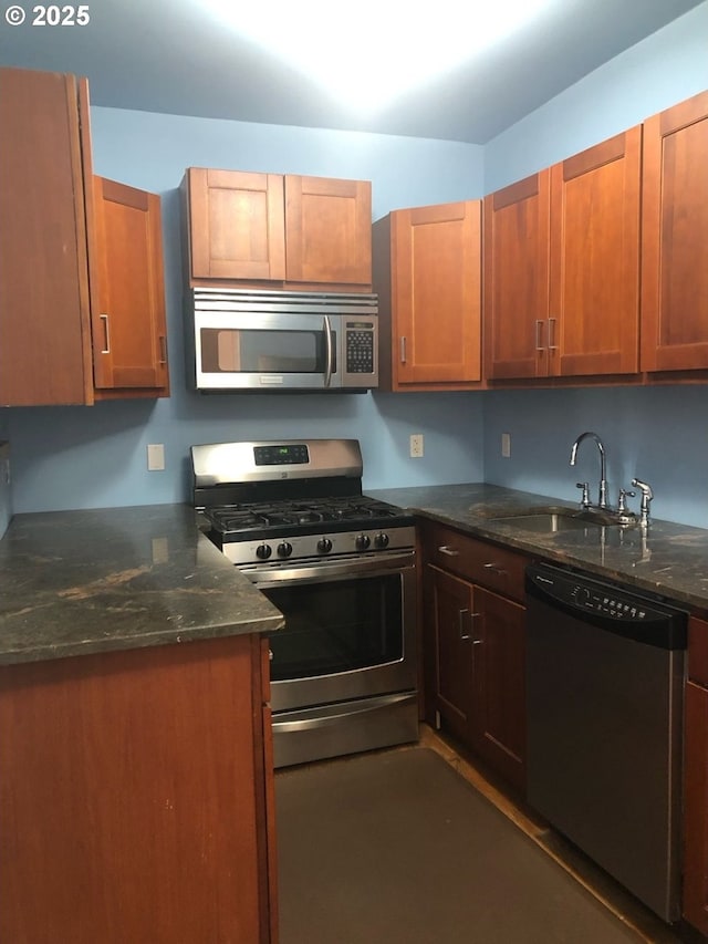 kitchen featuring dark stone countertops, appliances with stainless steel finishes, brown cabinetry, and a sink