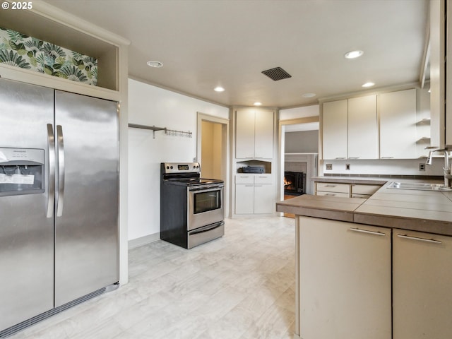 8978 SW Terreton Pl, Portland, OR 97223 - kitchen featuring appliances with stainless steel finishes, a sink, recessed lighting, a warm lit fireplace, and white cabinetry