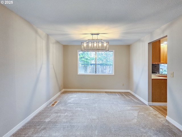 unfurnished dining area featuring light carpet, sink, and a textured ceiling