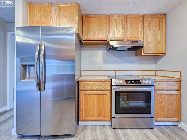 kitchen with a textured ceiling, light wood-type flooring, stainless steel appliances, and light brown cabinetry