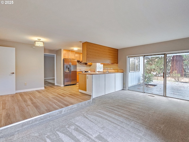 kitchen featuring light brown cabinets, sink, stainless steel fridge, light colored carpet, and kitchen peninsula