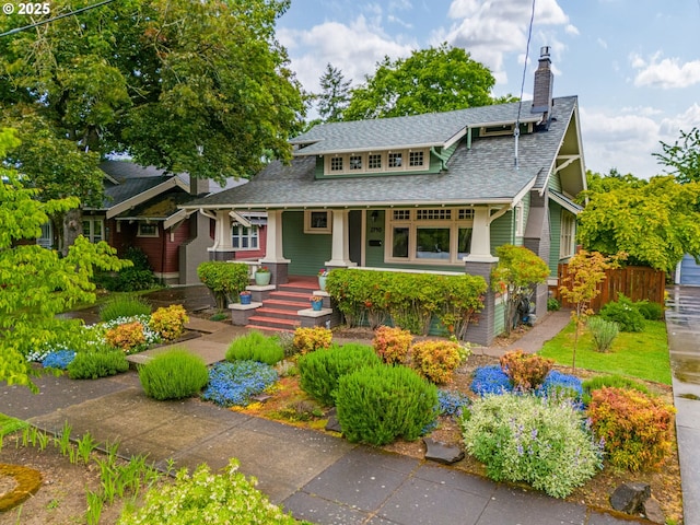view of front facade featuring a chimney, covered porch, a shingled roof, and fence