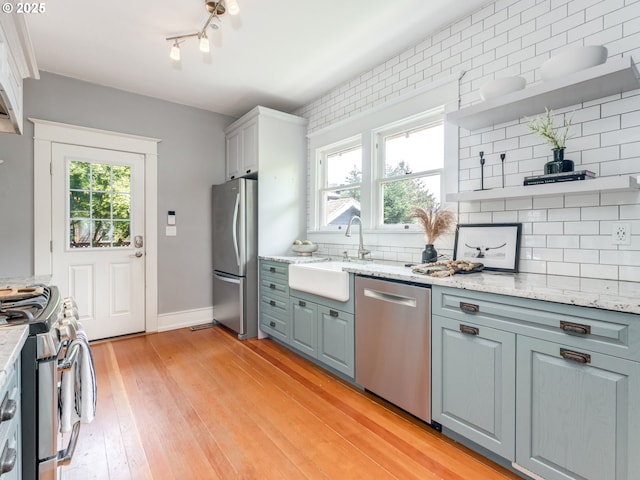 kitchen featuring appliances with stainless steel finishes, open shelves, a sink, backsplash, and light wood-style flooring