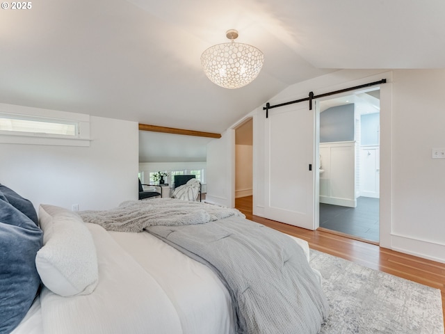 bedroom featuring a barn door, wood finished floors, lofted ceiling, multiple windows, and a walk in closet