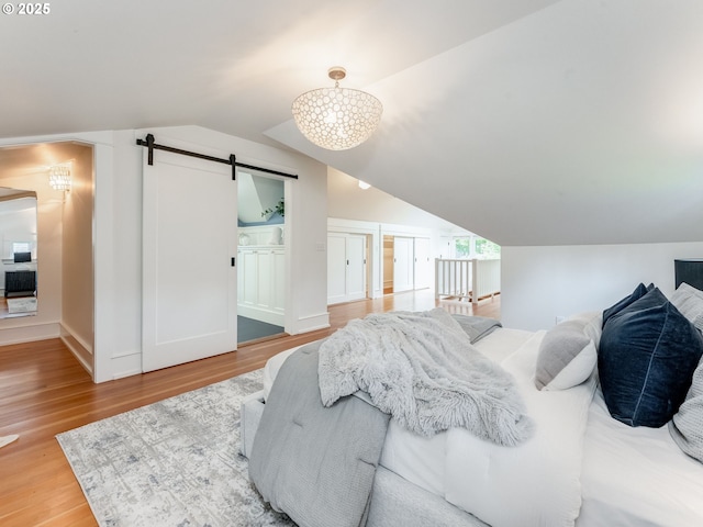 bedroom featuring a barn door, light wood-style floors, vaulted ceiling, and baseboards