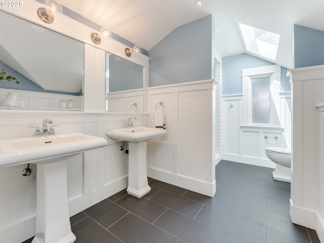 full bath with a decorative wall, a skylight, lofted ceiling, wainscoting, and toilet