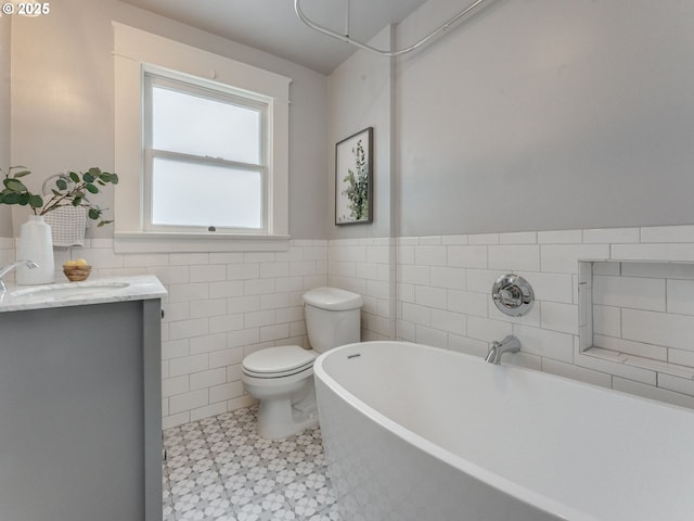 full bathroom featuring a freestanding tub, toilet, tile walls, a wainscoted wall, and vanity