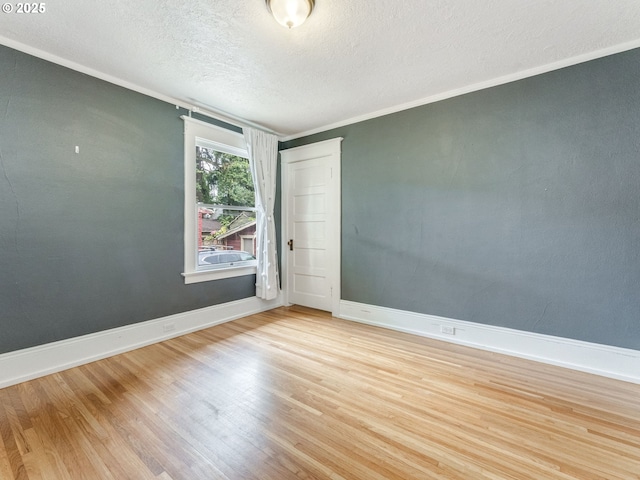 empty room featuring wood finished floors, a textured ceiling, baseboards, and crown molding