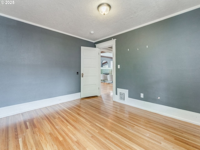 unfurnished room with wood finished floors, a textured ceiling, baseboards, and crown molding