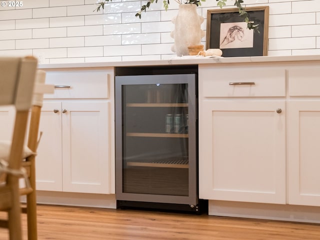 kitchen view of wine cooler, light wood-type flooring, light countertops, and white cabinetry