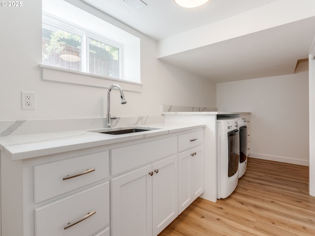 clothes washing area featuring separate washer and dryer, light wood finished floors, baseboards, and cabinet space