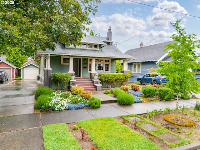 bungalow-style house with covered porch, a garage, an outbuilding, a chimney, and a shingled roof