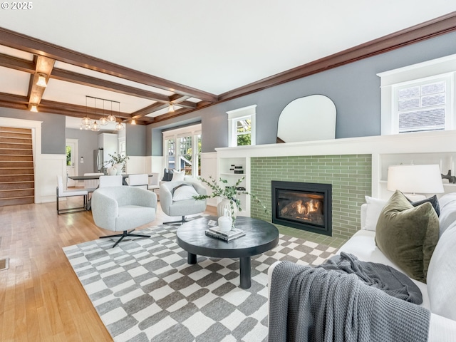 living room featuring coffered ceiling, wood finished floors, a glass covered fireplace, beam ceiling, and a wainscoted wall