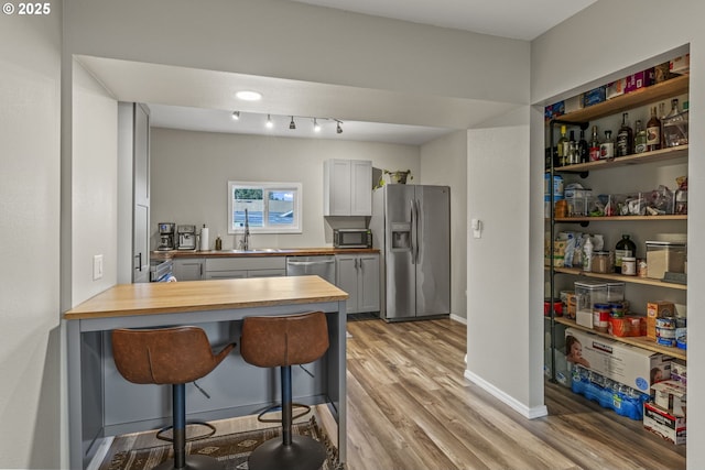 kitchen with appliances with stainless steel finishes, a kitchen bar, butcher block counters, kitchen peninsula, and light wood-type flooring