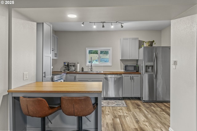 kitchen with gray cabinets, kitchen peninsula, sink, appliances with stainless steel finishes, and wood counters