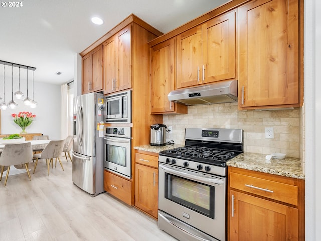 kitchen with hanging light fixtures, light wood-type flooring, appliances with stainless steel finishes, light stone countertops, and backsplash