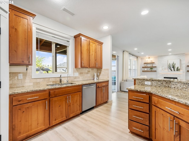 kitchen with light stone counters, sink, stainless steel dishwasher, and light wood-type flooring