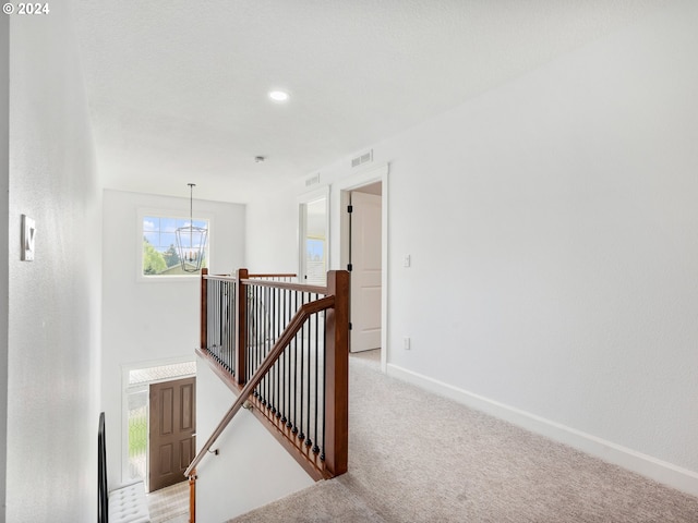 hallway featuring light carpet and a notable chandelier