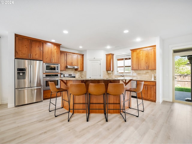 kitchen with appliances with stainless steel finishes, a center island, a breakfast bar area, and light stone counters