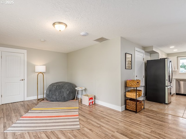 sitting room featuring baseboards, light wood-style floors, visible vents, and a textured ceiling